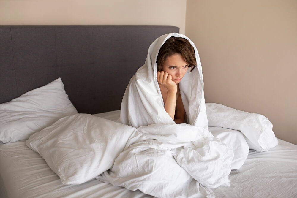 Person sitting awake in bed after panic attack during sleep, feeling tired and unable to sleep