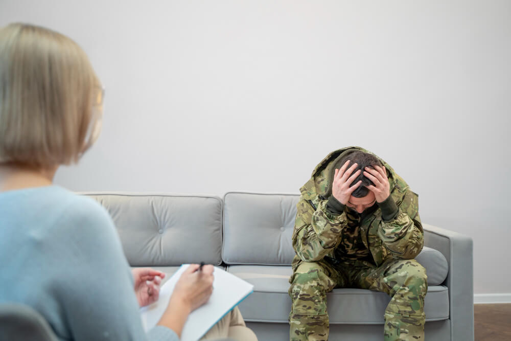veteran sitting with therapist sitting holding head with stress and burden signs of ptsd