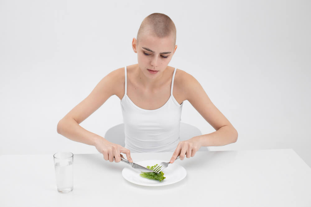 Young woman sitting alone looking emotionally distressed due to anorexia nervosa and mental health struggles.