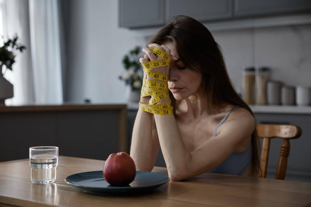 Young woman sitting alone looking emotionally distressed due to anorexia nervosa and mental health struggles.