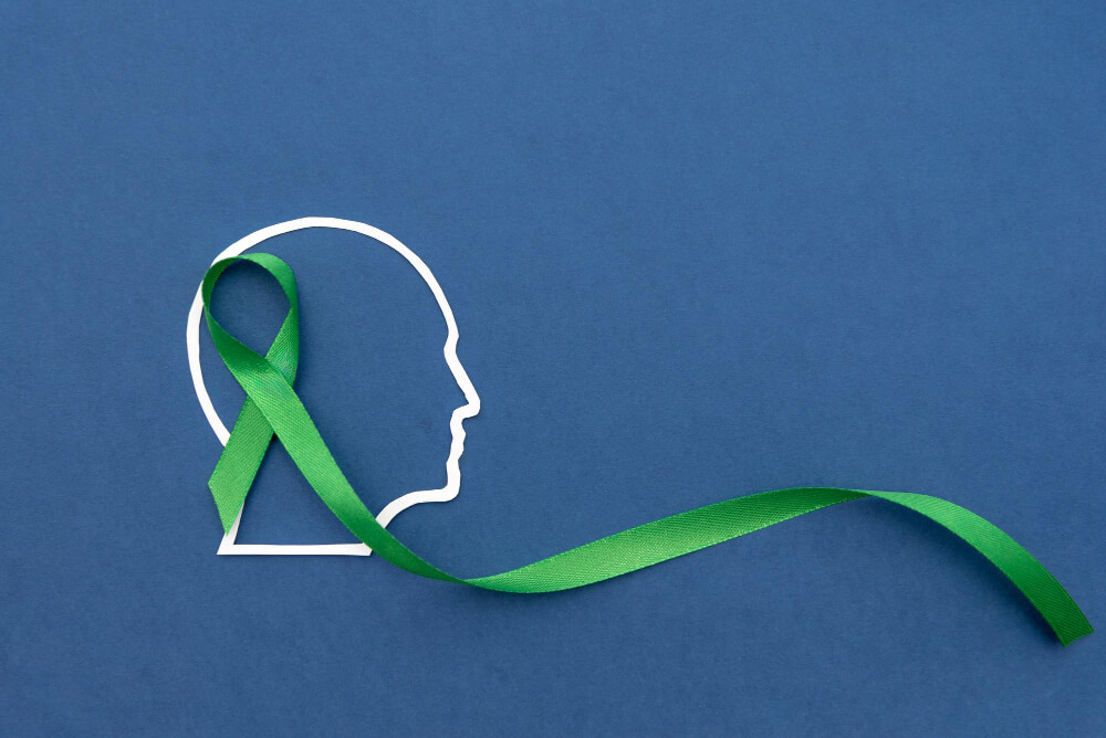 Green mental health awareness ribbon placed with human mind about emotional wellness and recovery.
